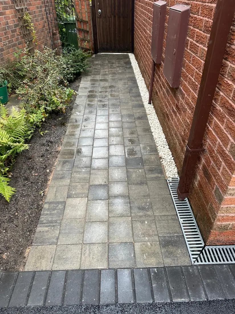Block paving side path with a linear drainage channel between a Cheshire house and boundary wall