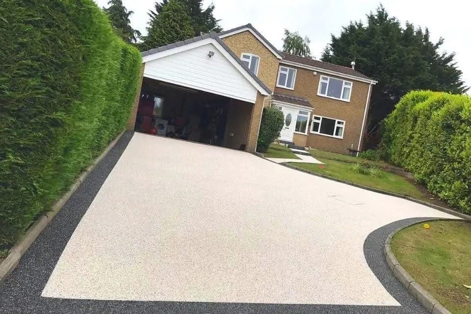 Wide resin bound driveway curving up to a detached Cheshire house behind a mature hedge