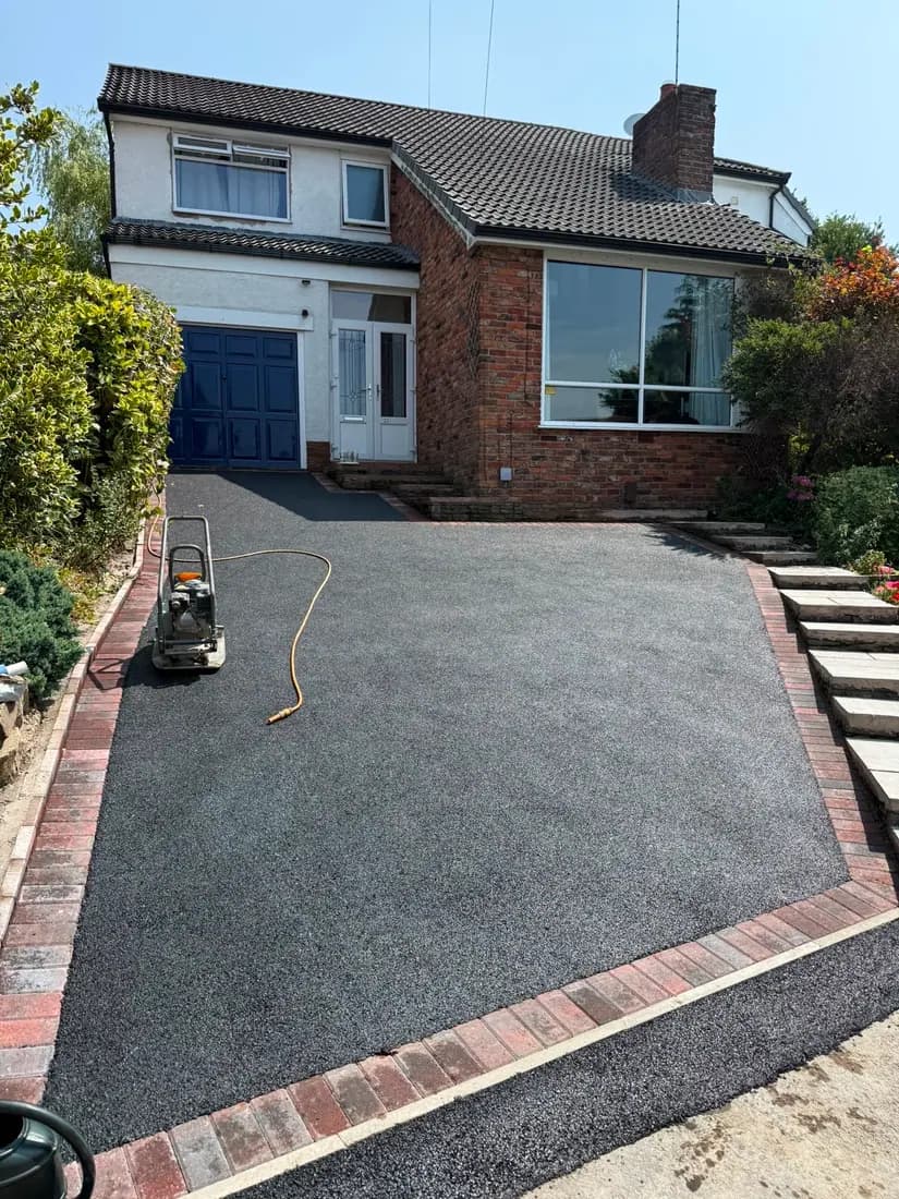 Tarmac driveway with a red brick edging course in front of a detached house